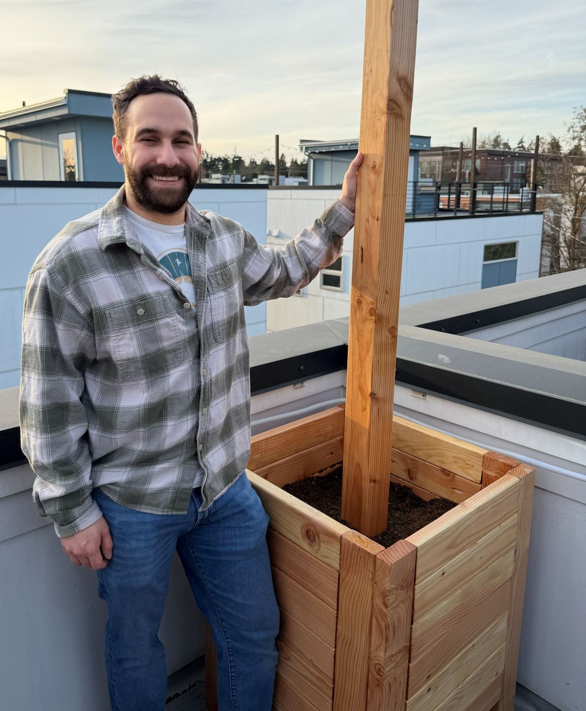 A person standing beside the planter for scale: the box reaches roughly hip height and the trellis post rises well above head height.